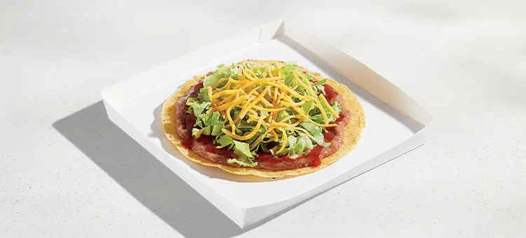 Tostada: Crispy tostada shell layered with savory refried beans, tangy red sauce, crispy lettuce and shredded cheese